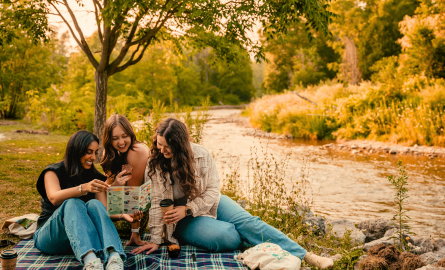 Three girls sitting on a blanket reading a map. The credit rivers runs behind them