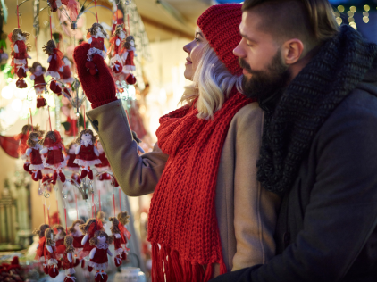 COUPLE LOOKING AT CHRISTMAS ORNAMENTS IN FRONT OF OUTDOOR MARKET DISPLAY.