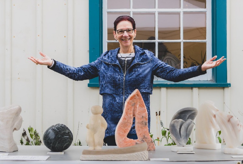 Artist behind a table filled with sculptures and ceramics