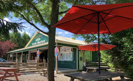 Allison's Farm Market A picture of a green barn with a sign on it that says Allison's Farm Market. In the foreground there is some picnic benches with red umbrellas