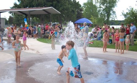 alot of kids playing at a splash pad on a sunny day