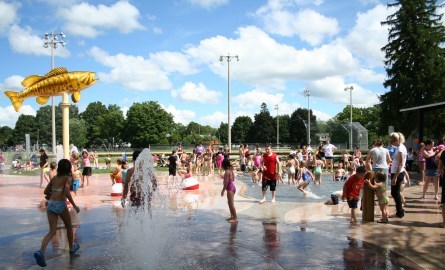a crowd of children playing at a splash pad on a sunny day