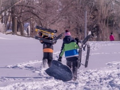 two people walking up a snowy hill with sleds