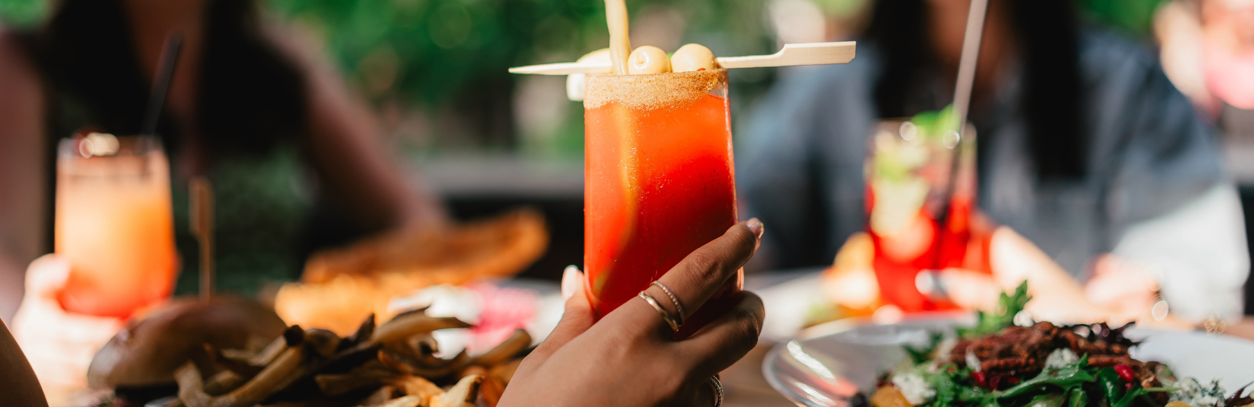 A hand holding a glass with a red drink inside of it